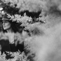A glamourous brunette wears a black hat, she is framed by the branches of frosty pine trees