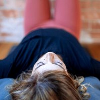 A woman in a yoga class lies on the mat with her legs up the wall. Her eyes are closed and only her head is funny in focus.