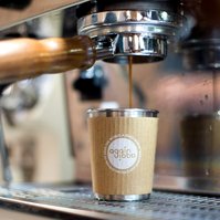 A reusable coffee cup sits under a machine as espresso drips into it