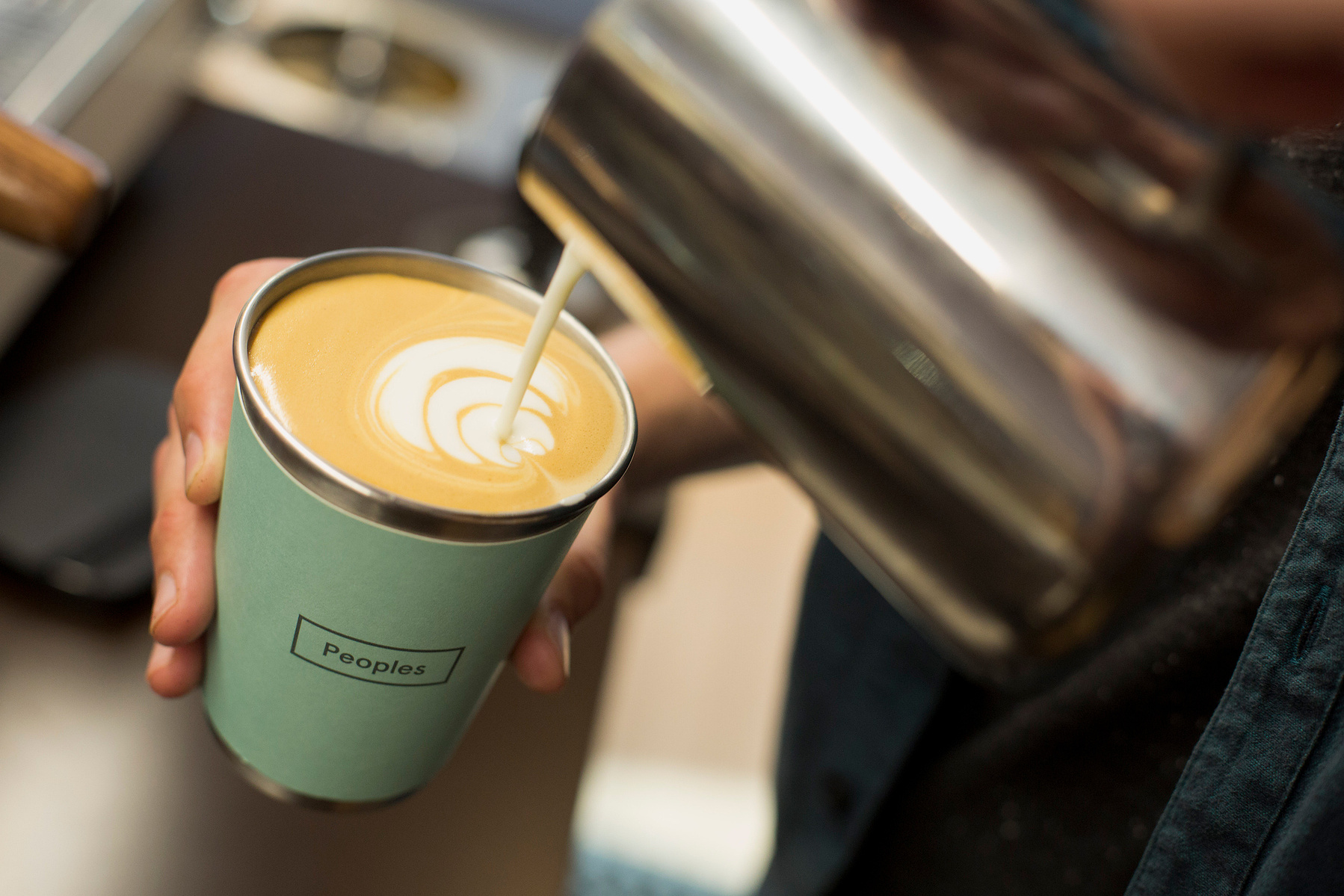 A barista pours milk into a cup of coffee