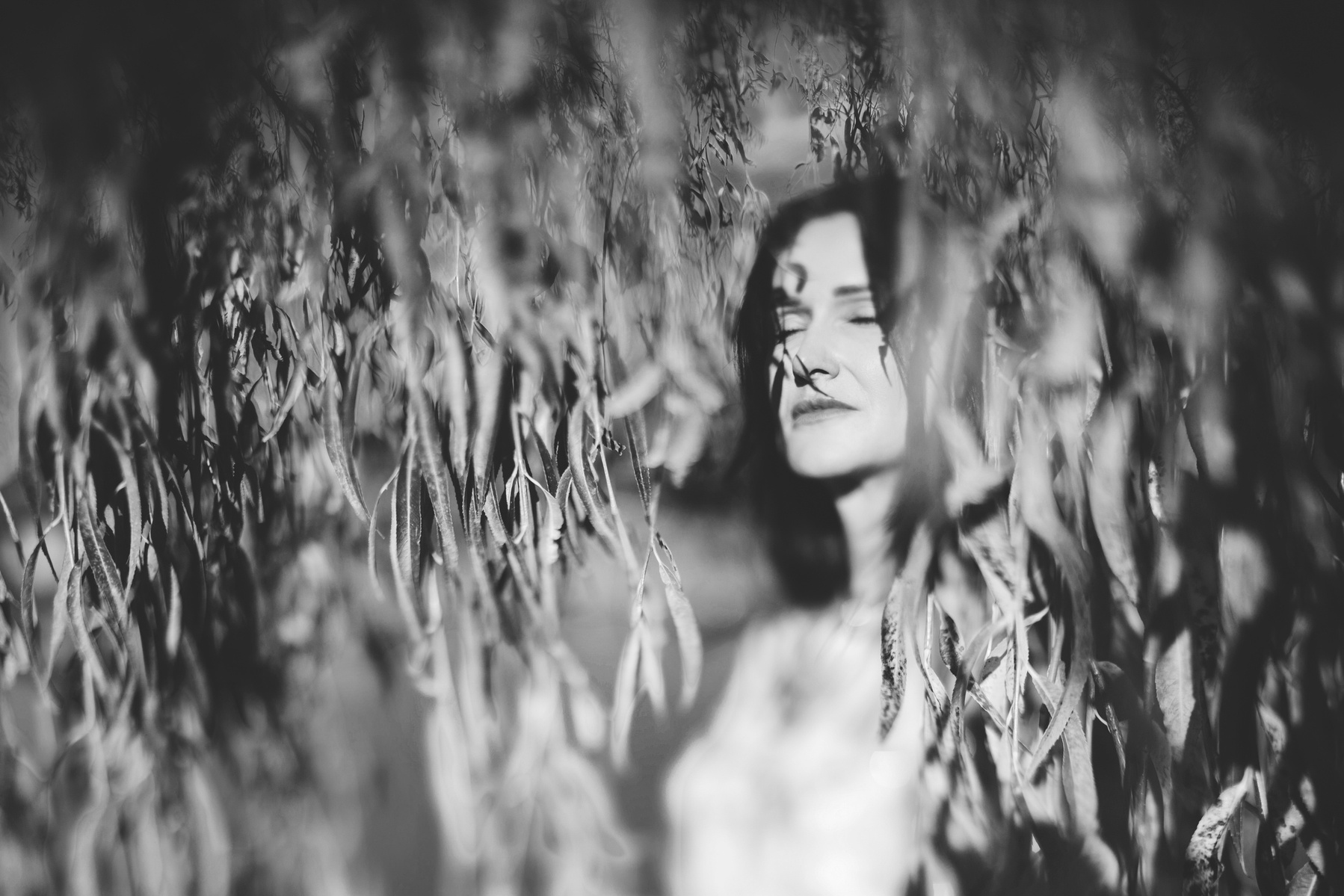 A brunette woman captured in a moment of stillness, she stands against a large tree and her eyes are closed in contemplation