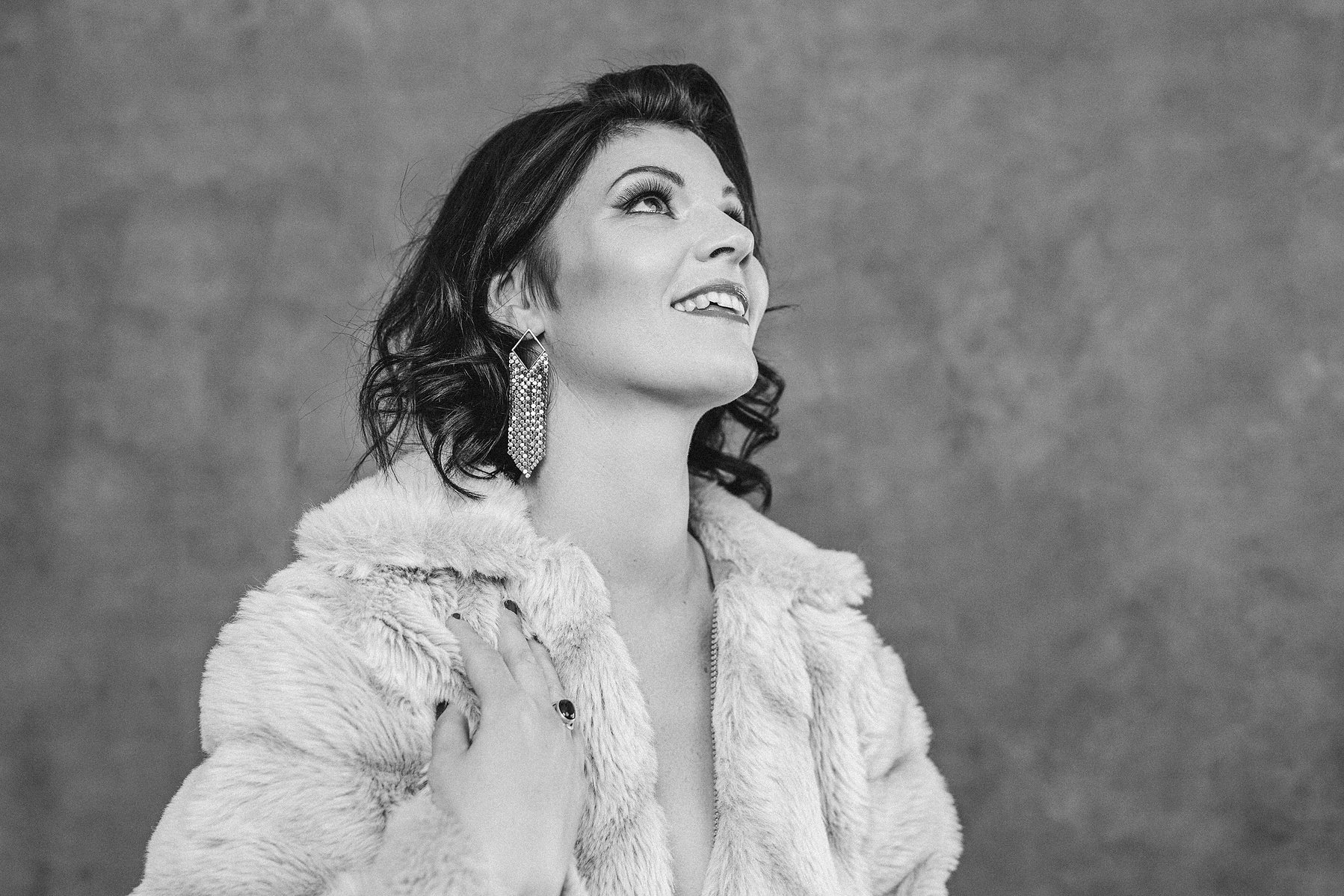 A brunette woman wears a fur coat, she is smiling enigmatically off camera