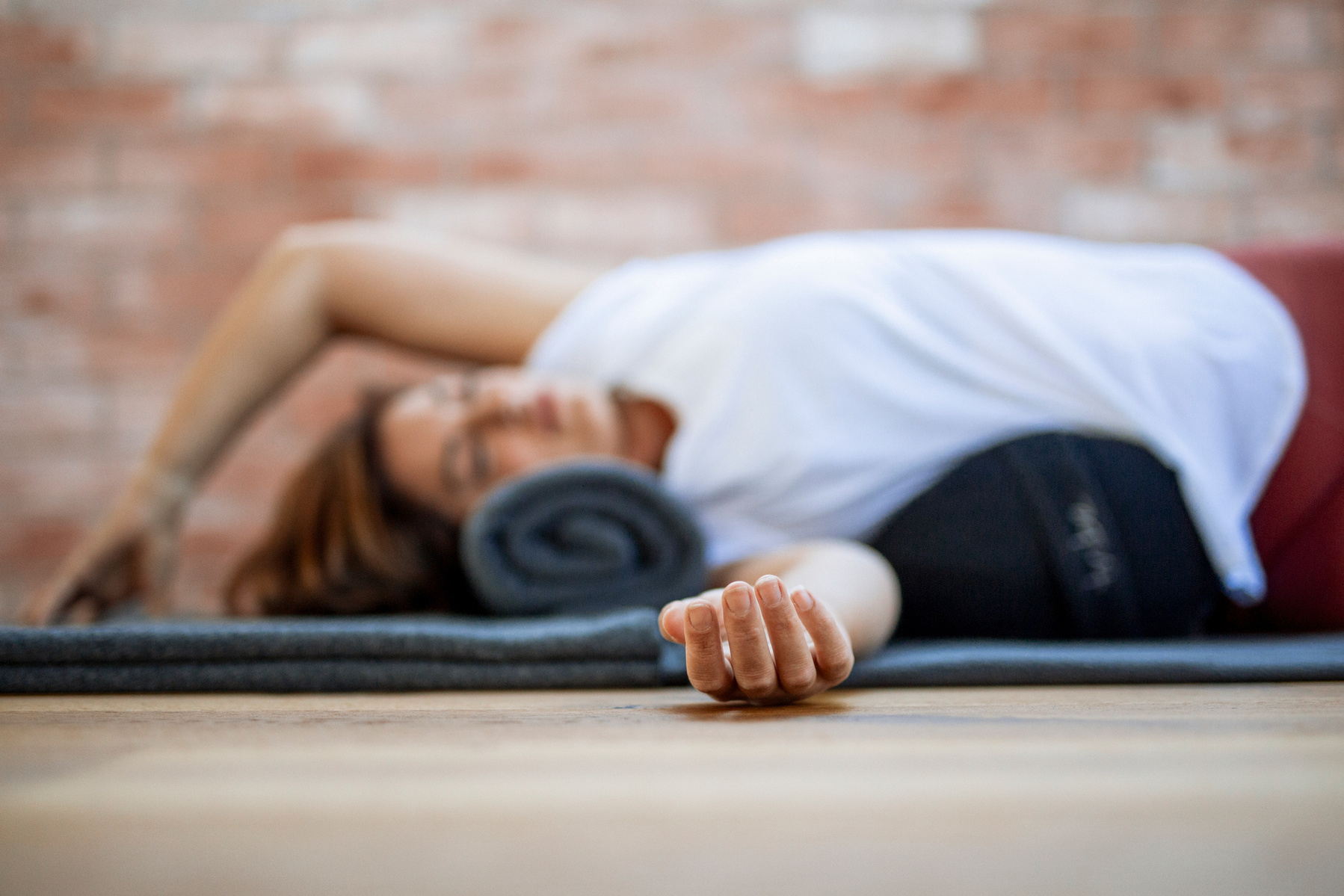 A woman lies on a yoga mat using props to help her stretch, one arm is out straight towards the camera and only her hand is fully in focus