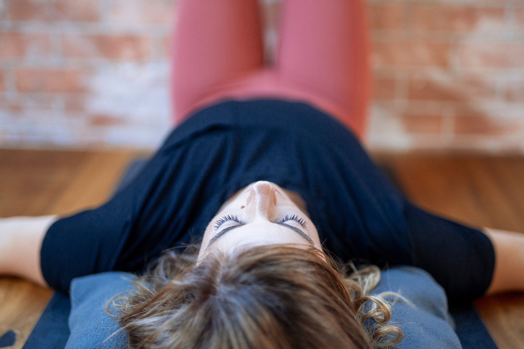 A woman in a yoga class lies on the mat with her legs up the wall. Her eyes are closed and only her head is funny in focus.