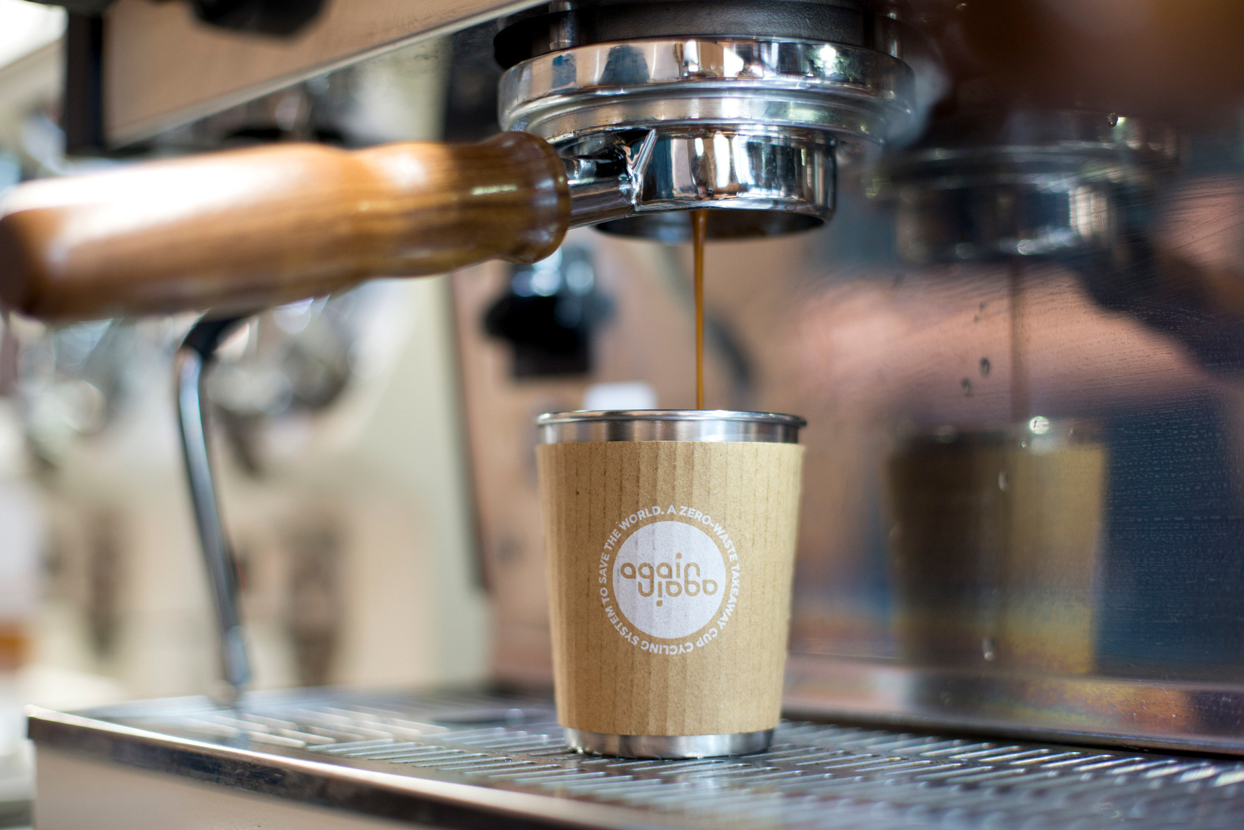 A reusable coffee cup sits under a machine as espresso drips into it