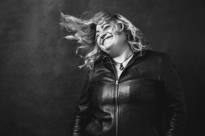 A curvy blonde woman wearing a leather jacket caught in movement, her hair flying away from her face