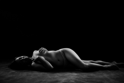 A naked woman lies on her side, one leg bent forward. She is covering her breasts with her hands and looking up