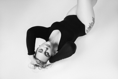A blonde woman wears a body suit, reclining on her back as she runs fingers through her hair