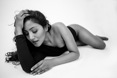A beautiful Indian woman lies on her front in a bodysuit with her head propped on a hand