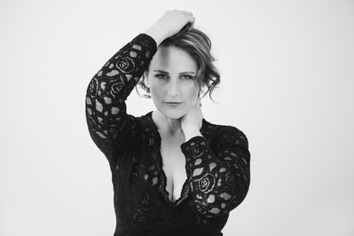 A striking woman wears a bodysuit as she stares into the camera, hands in her hair