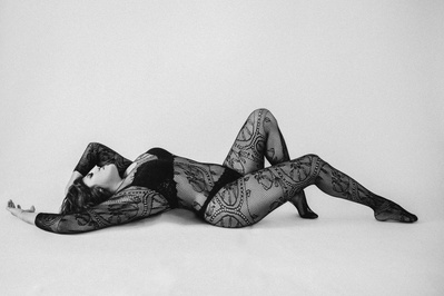 A curvaceous woman wears a full length bodysuit, reclining with arms above her head