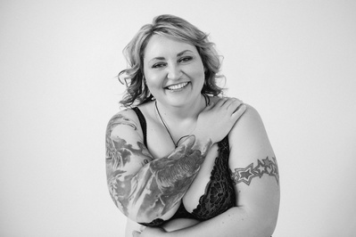 A curvaceous blonde woman with tattoos smiles at the camera