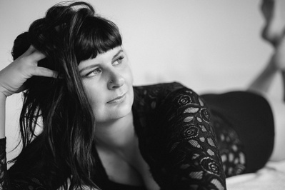 A woman with funky brown hair lays down on a bed with her head supported on a hand