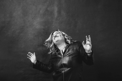 Blonde curvy woman wearing a leather jacket dances with her eyes wide