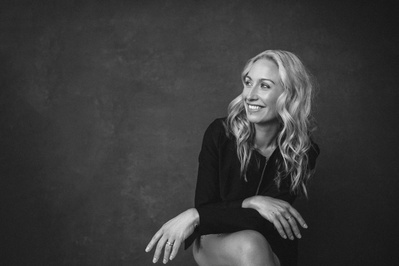 Blonde woman sits in a relaxed stance, hands crossed on her knees as she smiles off camera