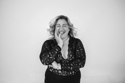 A blonde woman in a lace bodysuit bites a finger and laughs into the camera