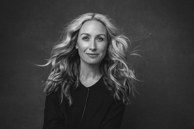 A middle aged woman with long blonde hair stares powerfully into the camera, her hair blown off her face