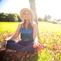 A blonde woman sits outside meditating, the bring sunshine filling the frame