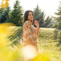 A brunette woman is framed by trees, the mountains of Queenstown visible behind her