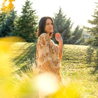 A brunette woman is framed by trees, the mountains of Queenstown visible behind her