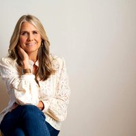 A glamourous older woman sits with her chin on a hand, smiling at the camera
