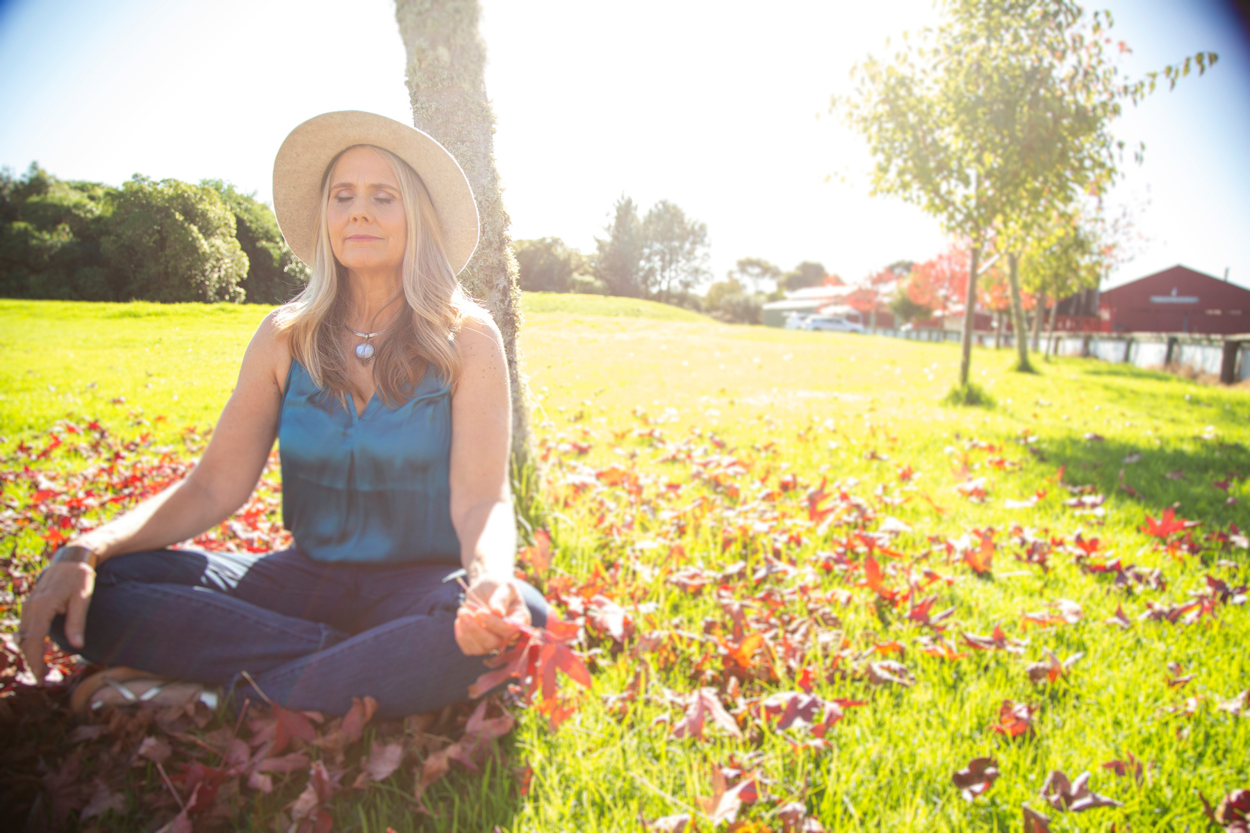 A blonde woman sits outside meditating, the bring sunshine filling the frame