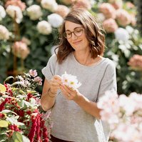 A healthy looking brunette woman smiles gently as she picks white flowers