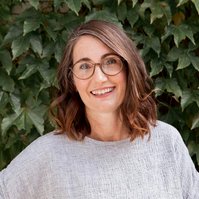 A portrait headshot of a healthy brunette woman standing in front of a wall of ivy