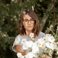 A brunette woman with shoulder length hair examine some white flowers