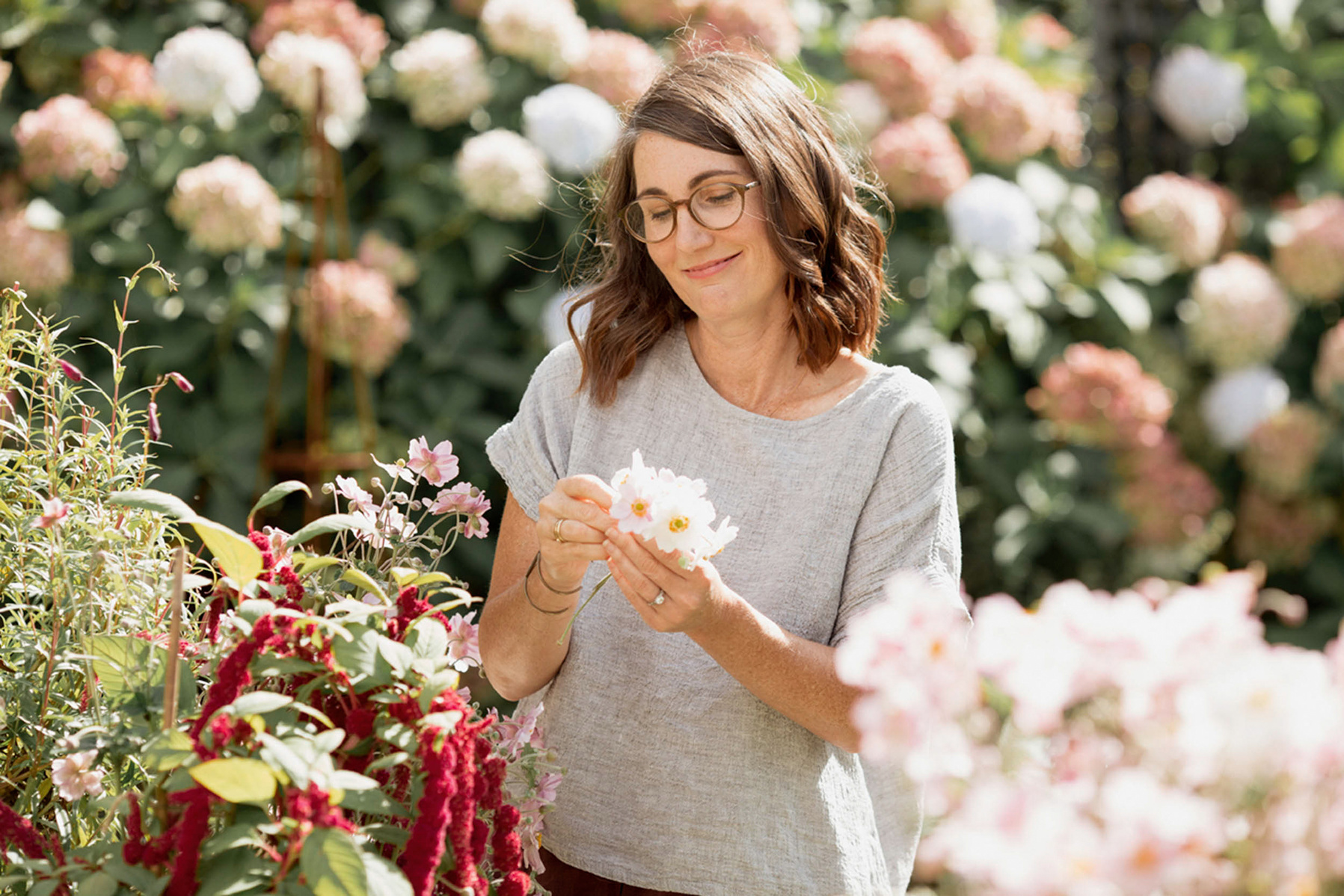 A healthy looking brunette woman smiles gently as she picks white flowers