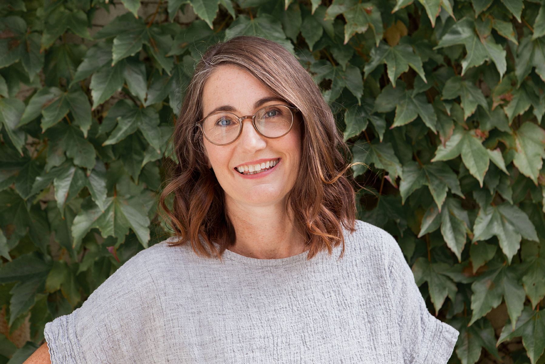 A portrait headshot of a healthy brunette woman standing in front of a wall of ivy