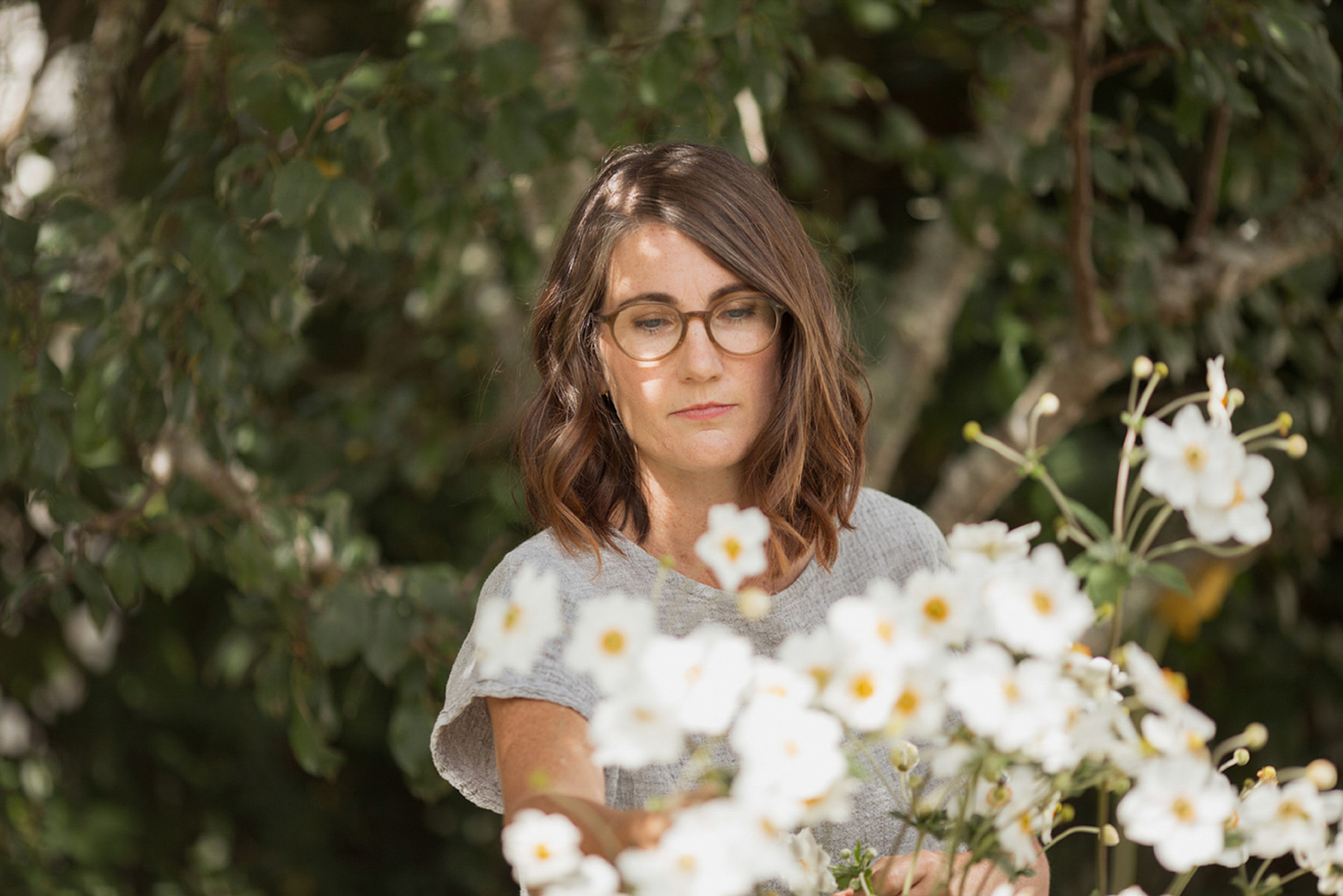 A brunette woman with shoulder length hair examine some white flowers