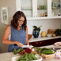 A woman stands in a kitchen chopping up fresh produce to cook into a nutritious meal 