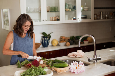 A slim woman stands in an airy kitchen, preparing a fresh and healthy meal
