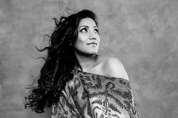 A beautiful woman wears a top showing one shoulder, her hair cascades down her back and she smiles enigmatically upwards