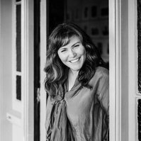 A brunette photographer peeks out of the door in a Nelson photography studio