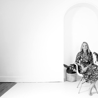 A slim blonder, older woman sits in a white chair and smiles at the camera