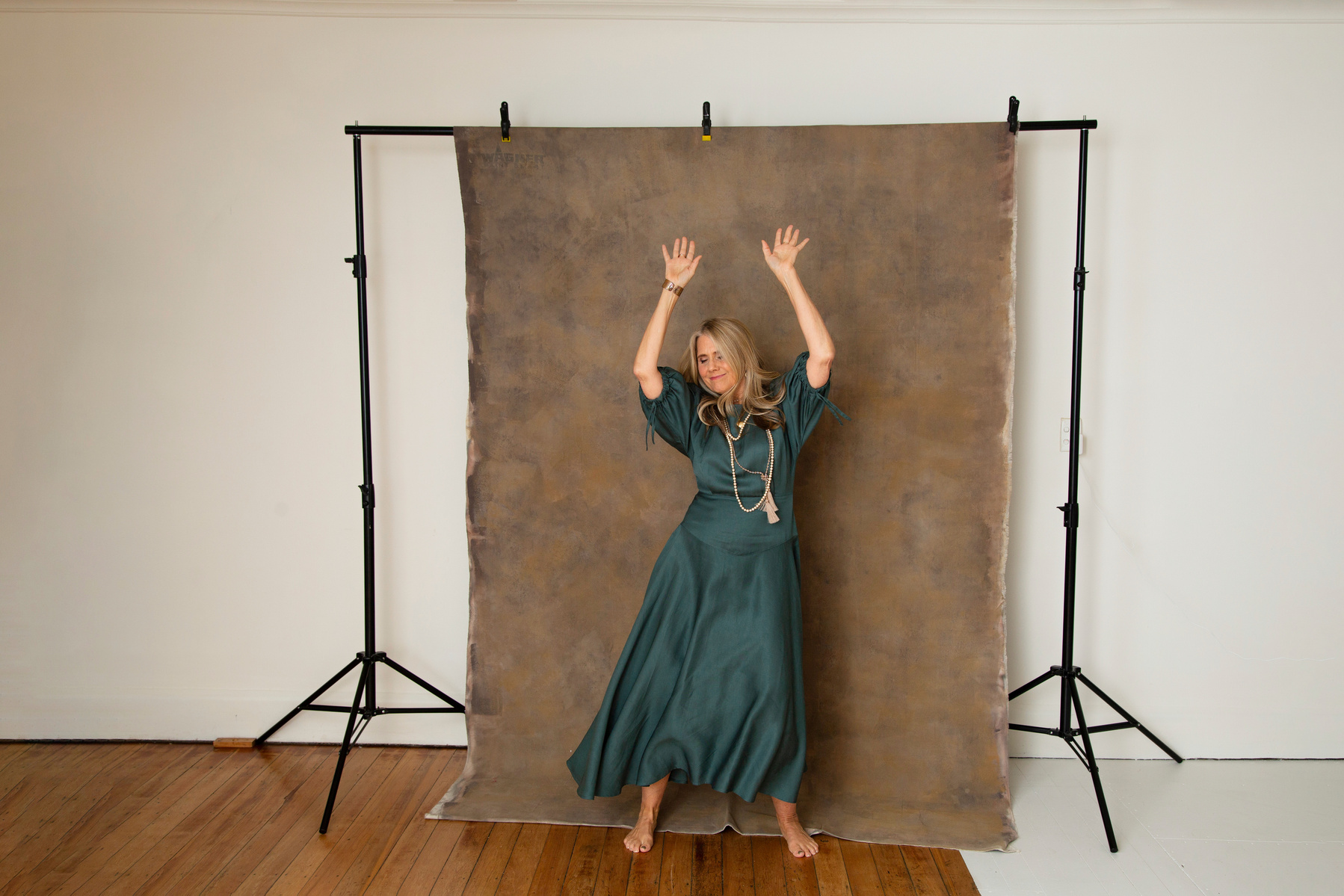 A slim blonde woman dances in front of a photography backdrop