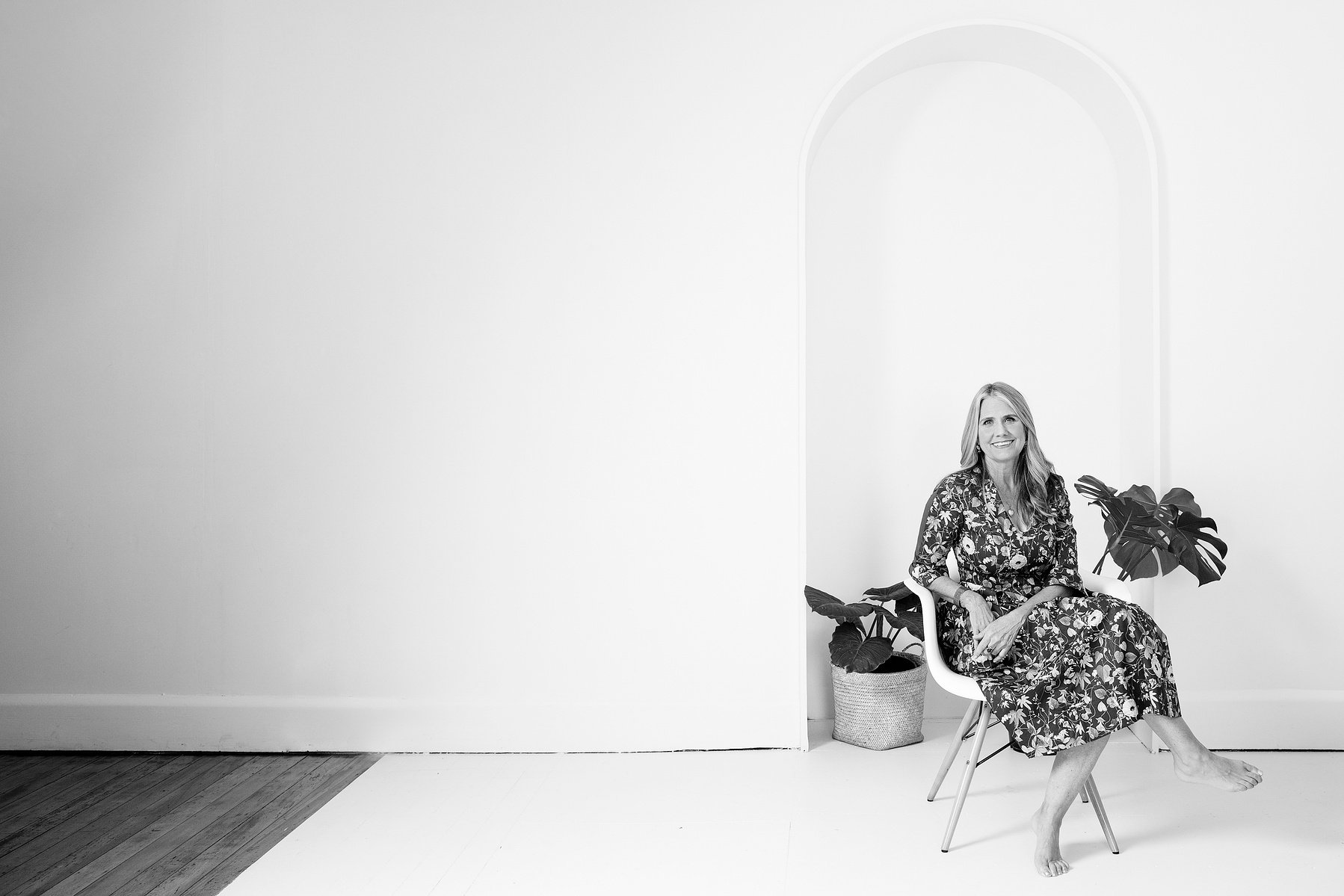 A slim blonder, older woman sits in a white chair and smiles at the camera