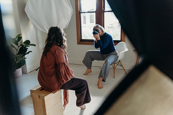 A photographer sits in a chair taking photos of a woman in a nelson photography studio
