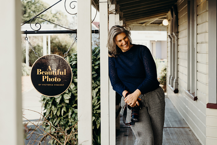 A tall, slim woman laughs on a quirky deck, holding a camera