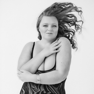 A young, curvy brunette woman flicks her long hair over her shoulder. 