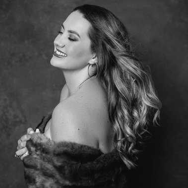 A young woman with long blond hair poses in a fur coat, hair thrown over her shoulder