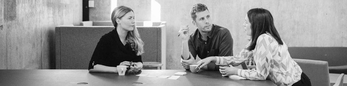 Three colleagues have a meeting, sitting around a table in a modern office space