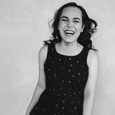 A slim young woman with brown hair is captured mid laugh