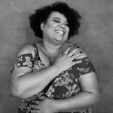 A curvaceous black woman is smiling widely as she hugs herself