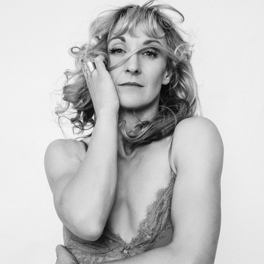 An older woman with blonde wavy hair and toned arms stares defiantly into the camera