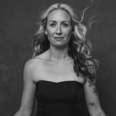 A slim woman with long blonde hair sits in the lotus position staring into the camera