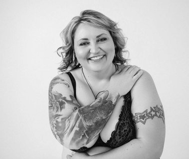 A curvy woman in lingerie hugging herself and looking really happy. 