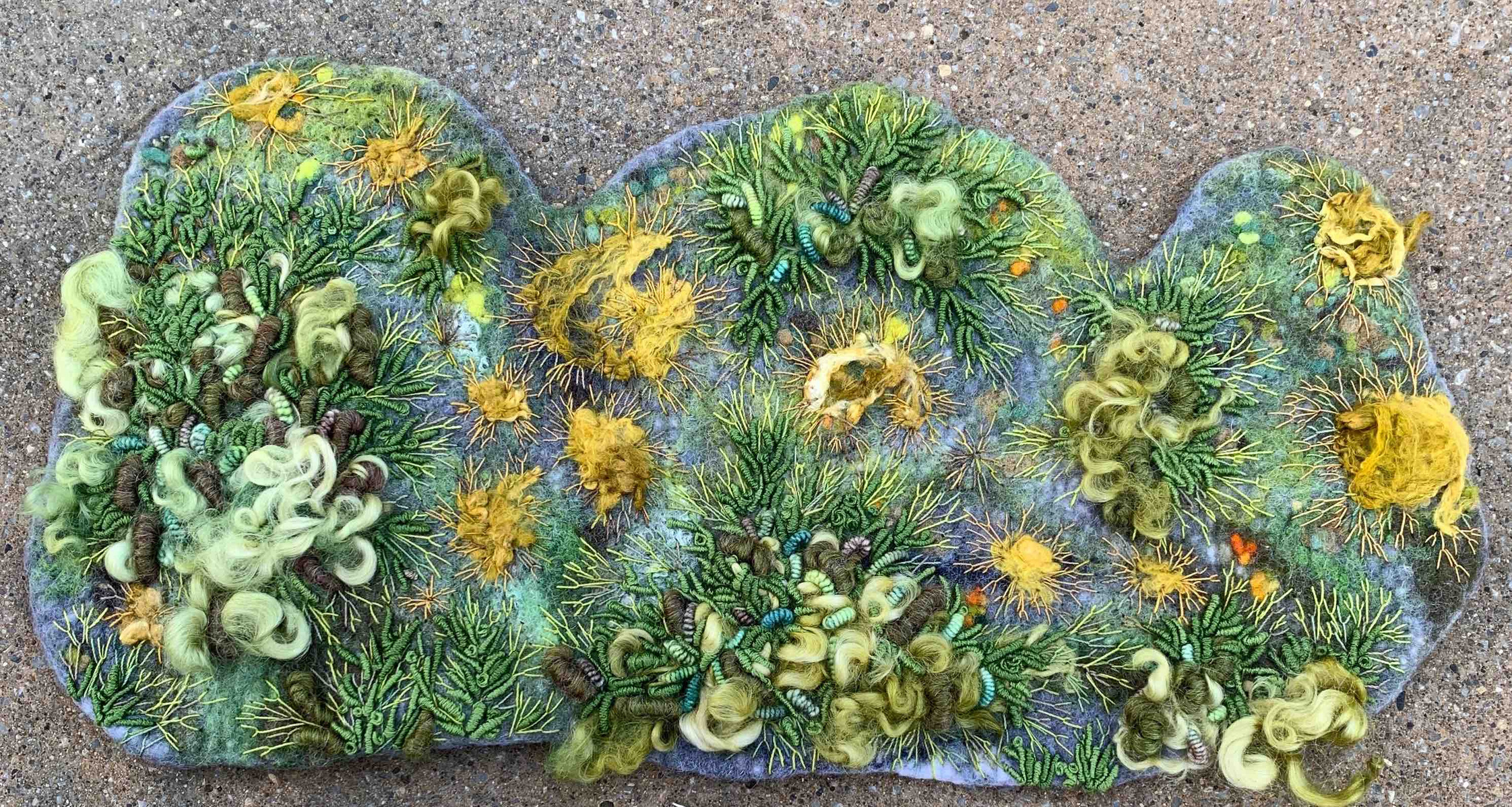 Wet felted textile art. The felt artist Lynn Comley has created a moss and lichen study in stitch on a piece of hand crafted wool felt.